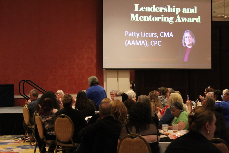 Leadership & Mentoring Award a crowd in front of a projector screen that reads "Leadership and Mentoring Award Patty Licurs, CMA (AAMA), CPC"
